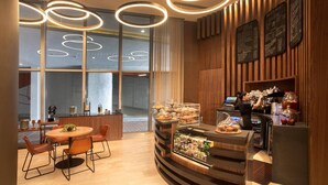 Una cafetería moderna con interior de madera, una barra con pasteles y un barista preparando bebidas.