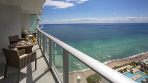 Un balcón con mobiliario de mimbre, una mesa con una bebida y vistas al océano y la playa.