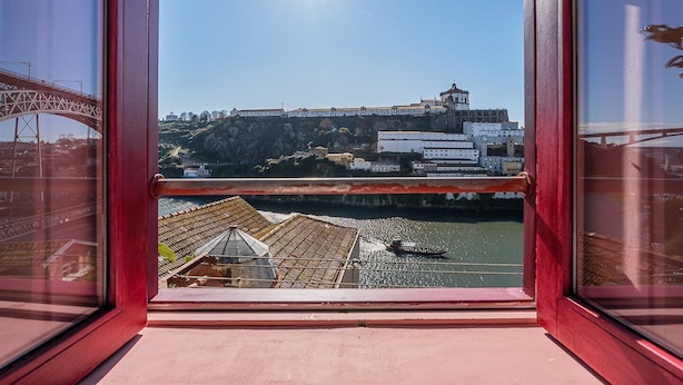 Blick aus einem Fenster auf einen Fluss mit einer Brücke und Gebäuden im Hintergrund.