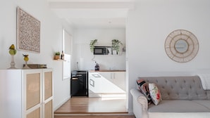 Ein modernes Wohnzimmer mit einer grauen Couch, einer Küche im Hintergrund und Dekoration an den Wänden.