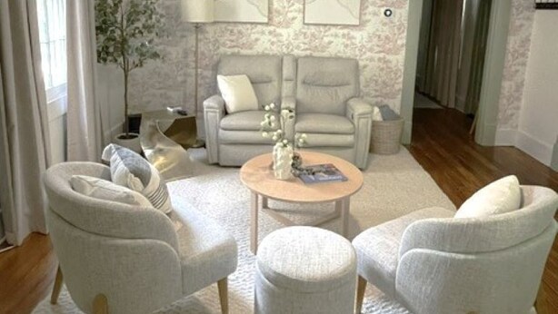 Una sala de estar con ventilador de techo, dos sillones, una mesa de centro redonda y una lámpara.