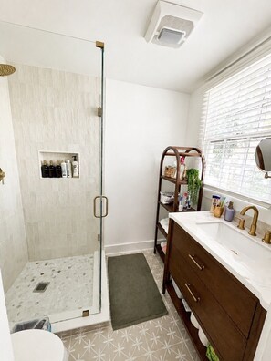 Un baño con cabina de ducha de vidrio, tocador con lavabo y ventana con persianas.