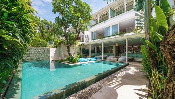 A modern pool area with a clear pool, surrounded by lush greenery and a multi-level building with outdoor seating. - 5 Star Villa with 5 Bedrooms, Bali Villa 2178 (Bali)