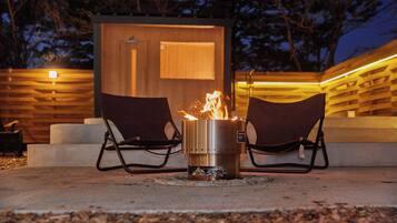 A fire pit with two chairs in front, set against a wooden wall with a door.