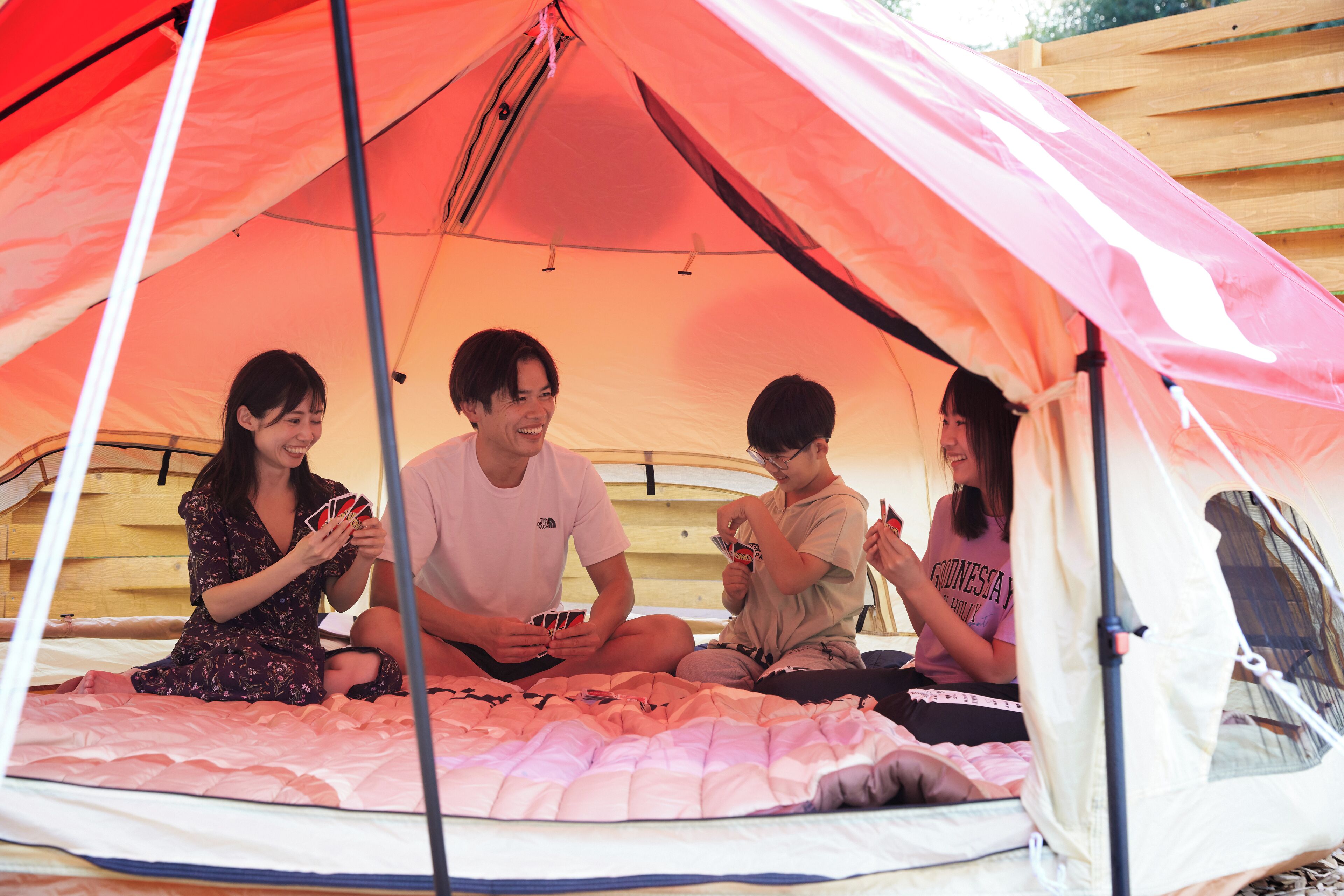 A group of people sitting inside a tent with a bed and blankets.