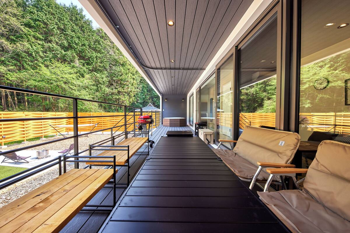 Terraza cubierta al aire libre con bancos de madera y un sofá, con vista a un área boscosa.