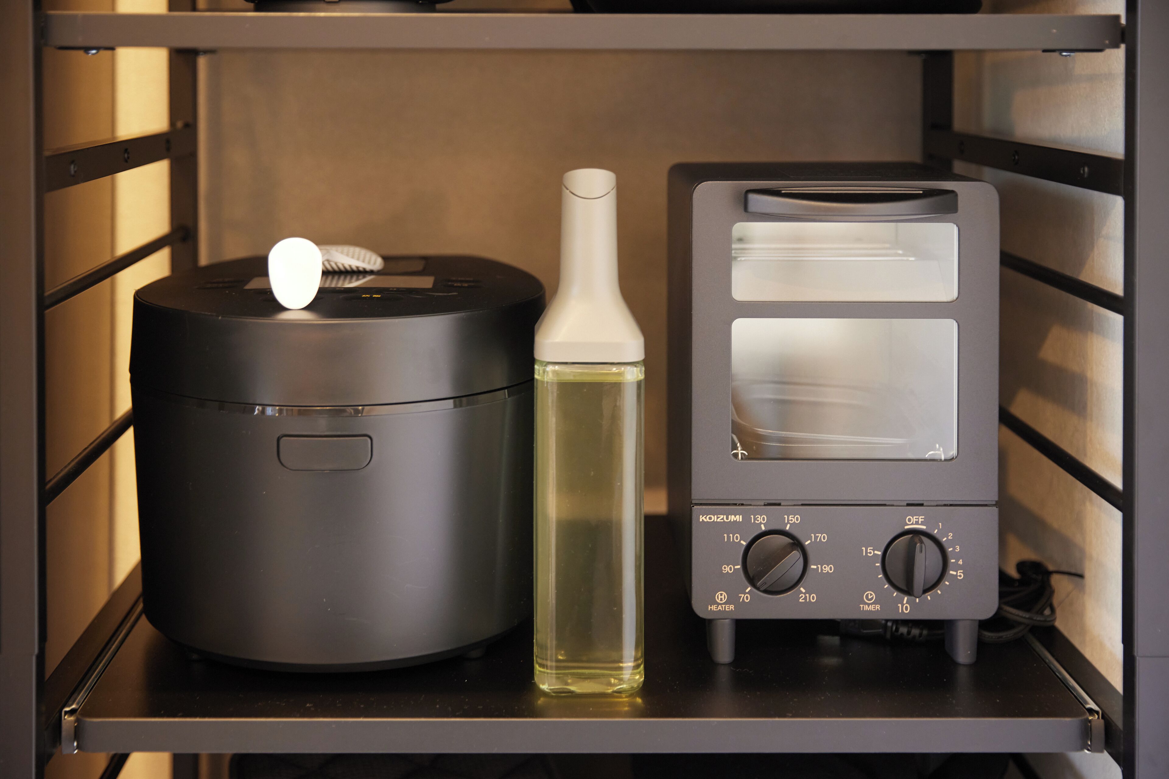 A kitchen with a rice cooker, a bottle of cooking oil, and a toaster.