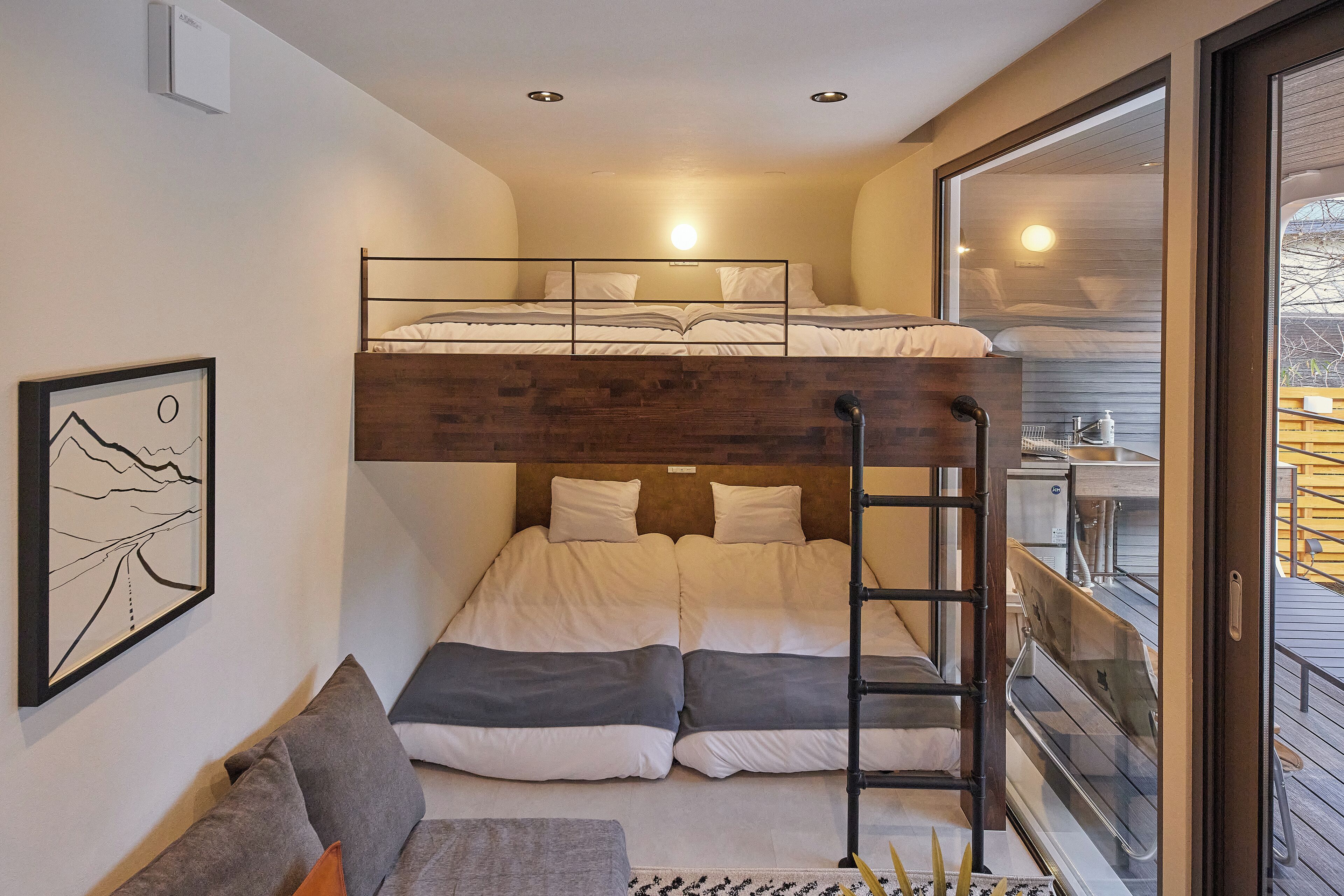 A compact room with a bunk bed, a sofa, and a ladder leading to a balcony.
