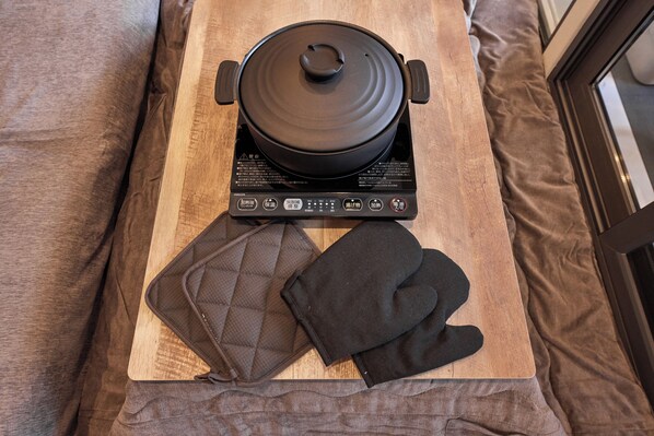 A portable electric stove with a pot on it, a quilted oven mitt, and a wooden cutting board. - IZA GLAMPING Chihaya-Akasaka Village (Chihayaakasaka-mura)