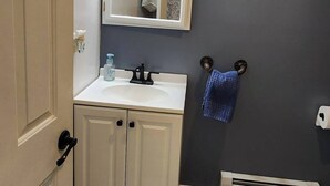 Ein Badezimmer mit weißem Waschtisch, einem beleuchteten Spiegel, einem Handtuchhalter und einer Heizung.
