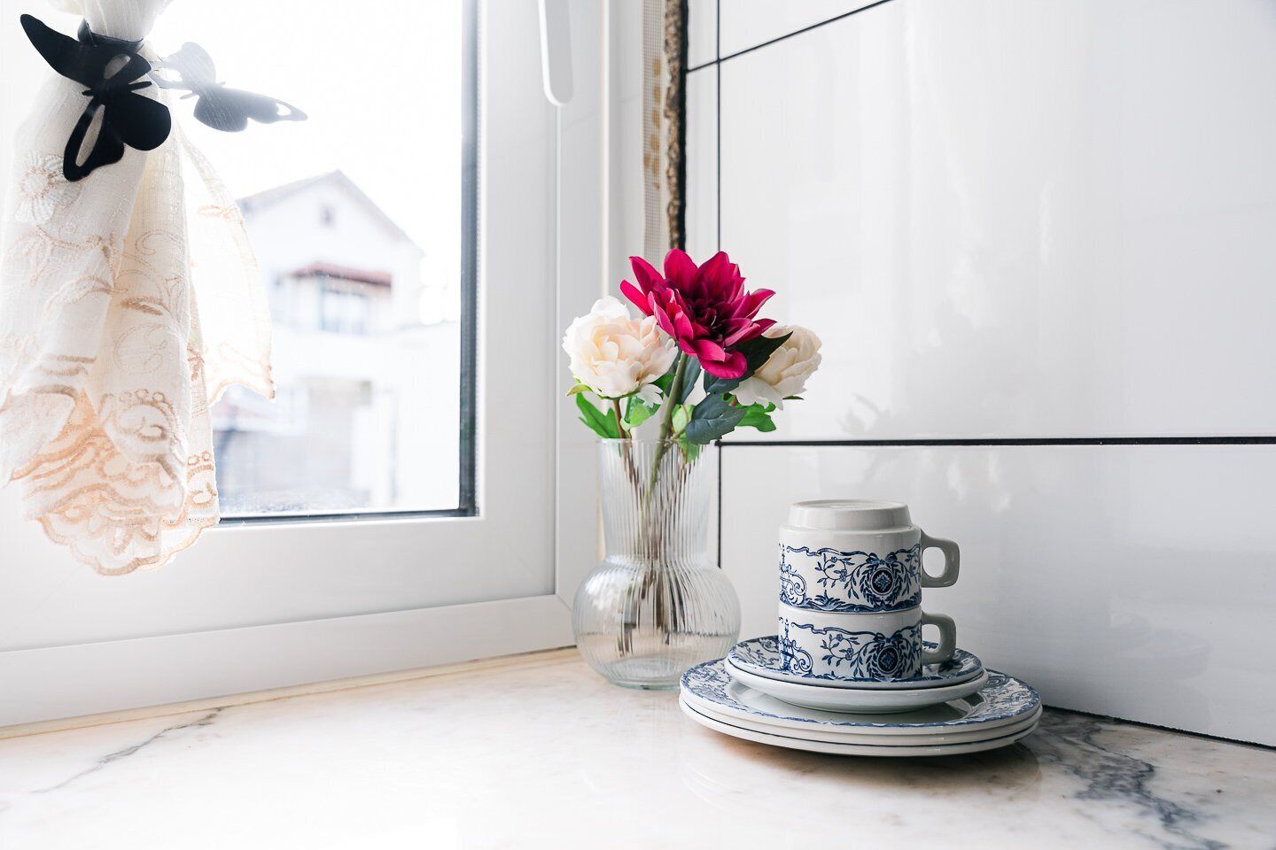 A kitchen with a window, a vase with flowers, and a tea set on the counter.