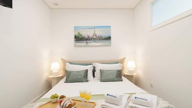 A hotel room with a bed, pillows, a tray with food and drinks, a painting of the Eiffel Tower, and a window.