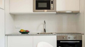 A modern kitchen with white cabinets, a stainless steel microwave, a sink, and a dining area with a table set for two.