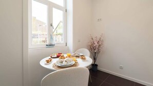 A dining area with a table set for breakfast, a window with a view of buildings, and a vase with flowers.