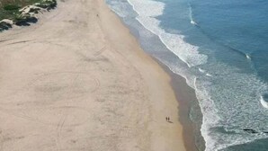 An aerial view of a coastal area with a sandy beach, a curved shoreline, and a distant city skyline.