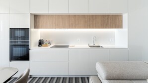 A modern kitchen with white cabinetry, a wooden accent panel, built-in appliances, and a minimalist design.