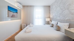 A modern hotel room with a large bed, a painting on the wall, a window with curtains, and a textured wall design.