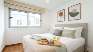 Un lit bien fait, avec un plateau contenant des éléments de petit-déjeuner, une fenêtre avec des rideaux et deux œuvres d’art encadrées accrochées au mur.