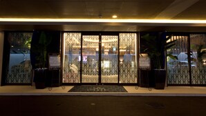 Entrada de hotel con puertas de vidrio con diseño, plantas en macetas y un cartel.