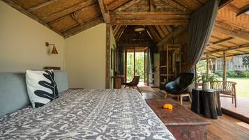 A bedroom with a large bed, a wooden ceiling, a view of the outdoors, and a small table with a plant.