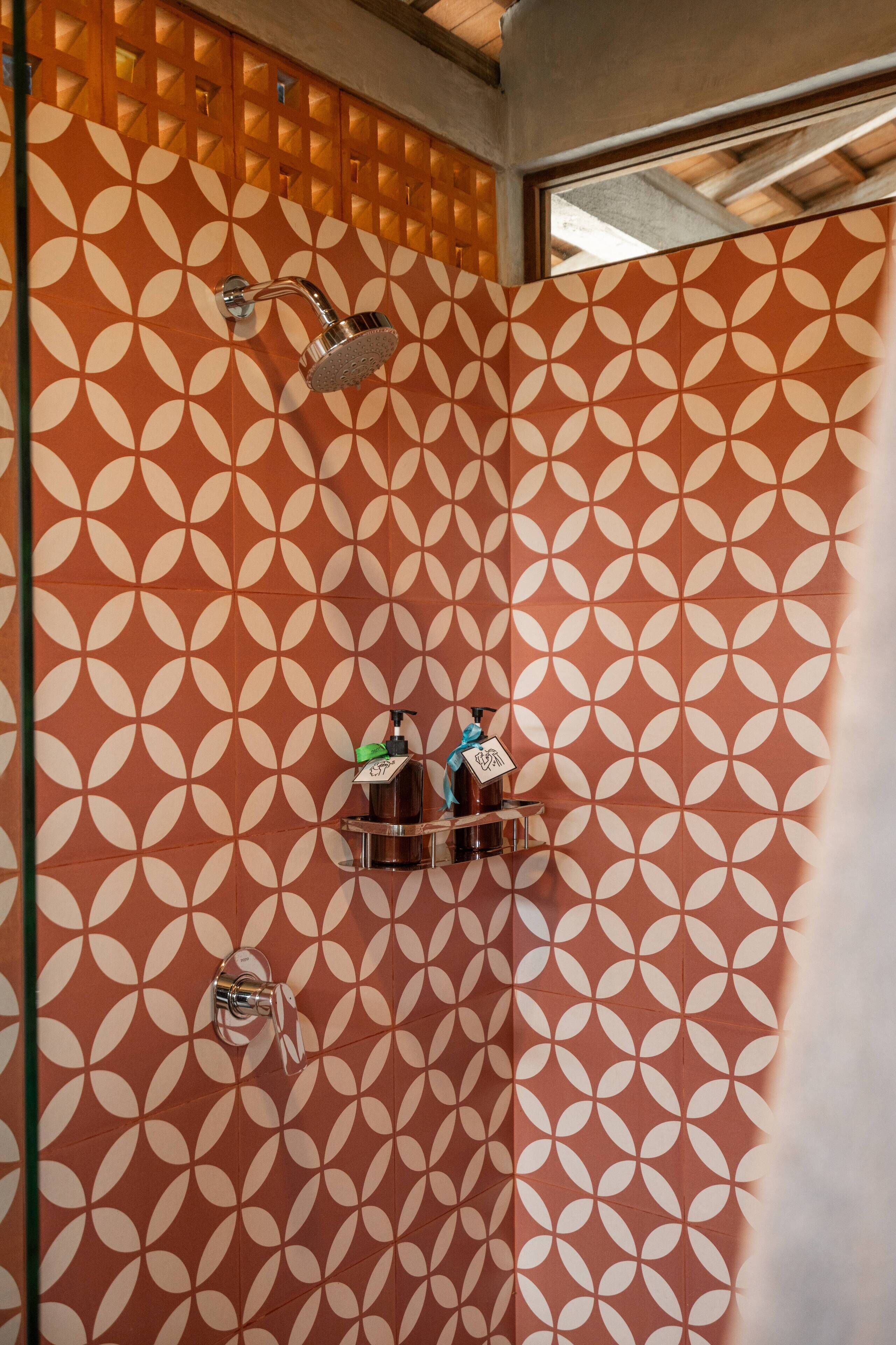 A bathroom with a patterned wall, a showerhead, and a soap dispenser.
