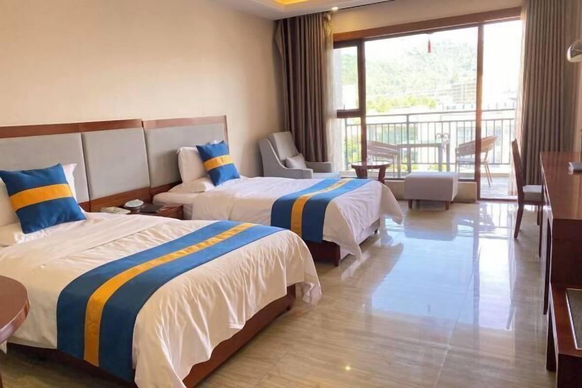 A hotel room with two beds, a balcony, a desk, and a chair.
