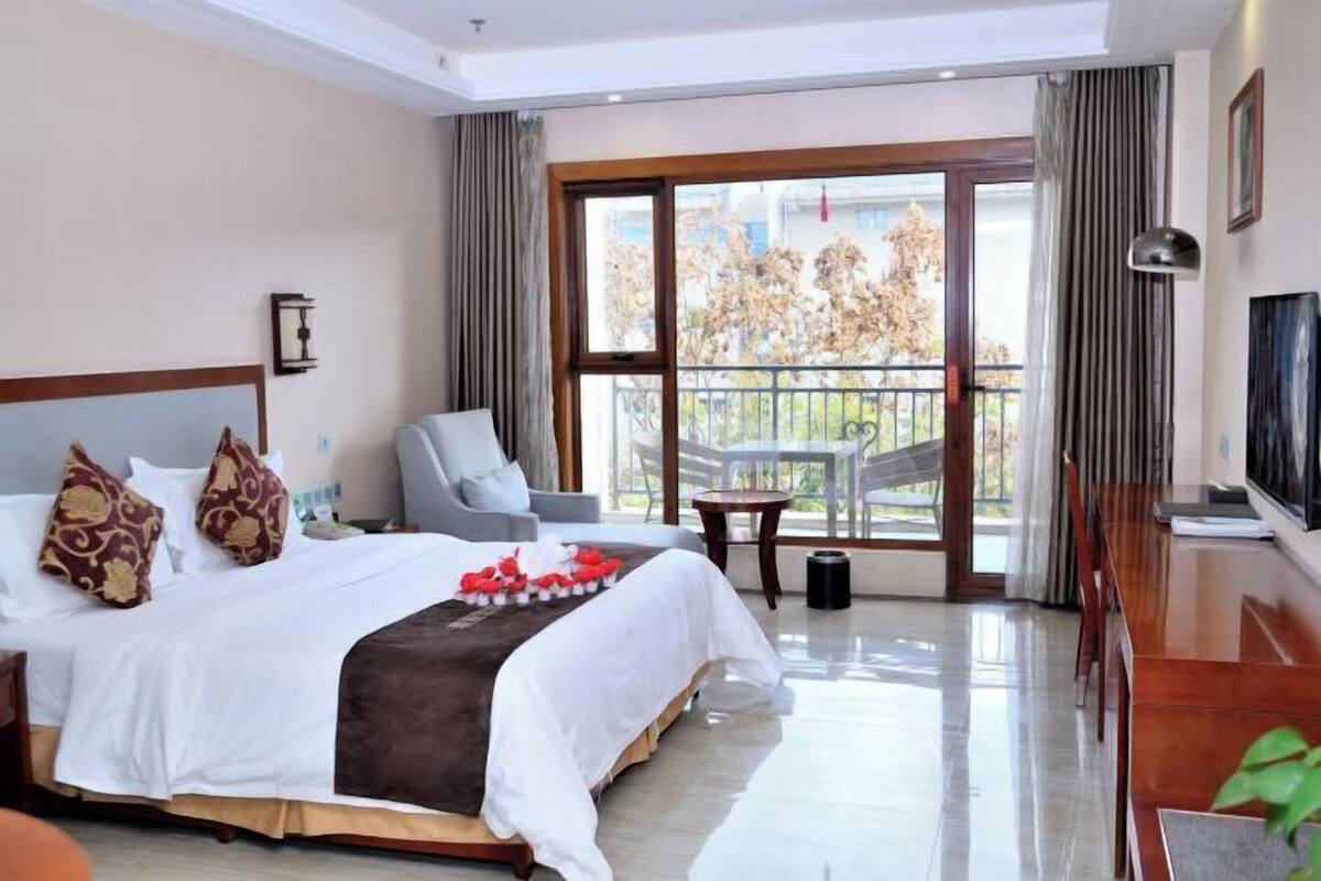 A hotel room with a bed, a TV, a balcony with a view, and a dining area.