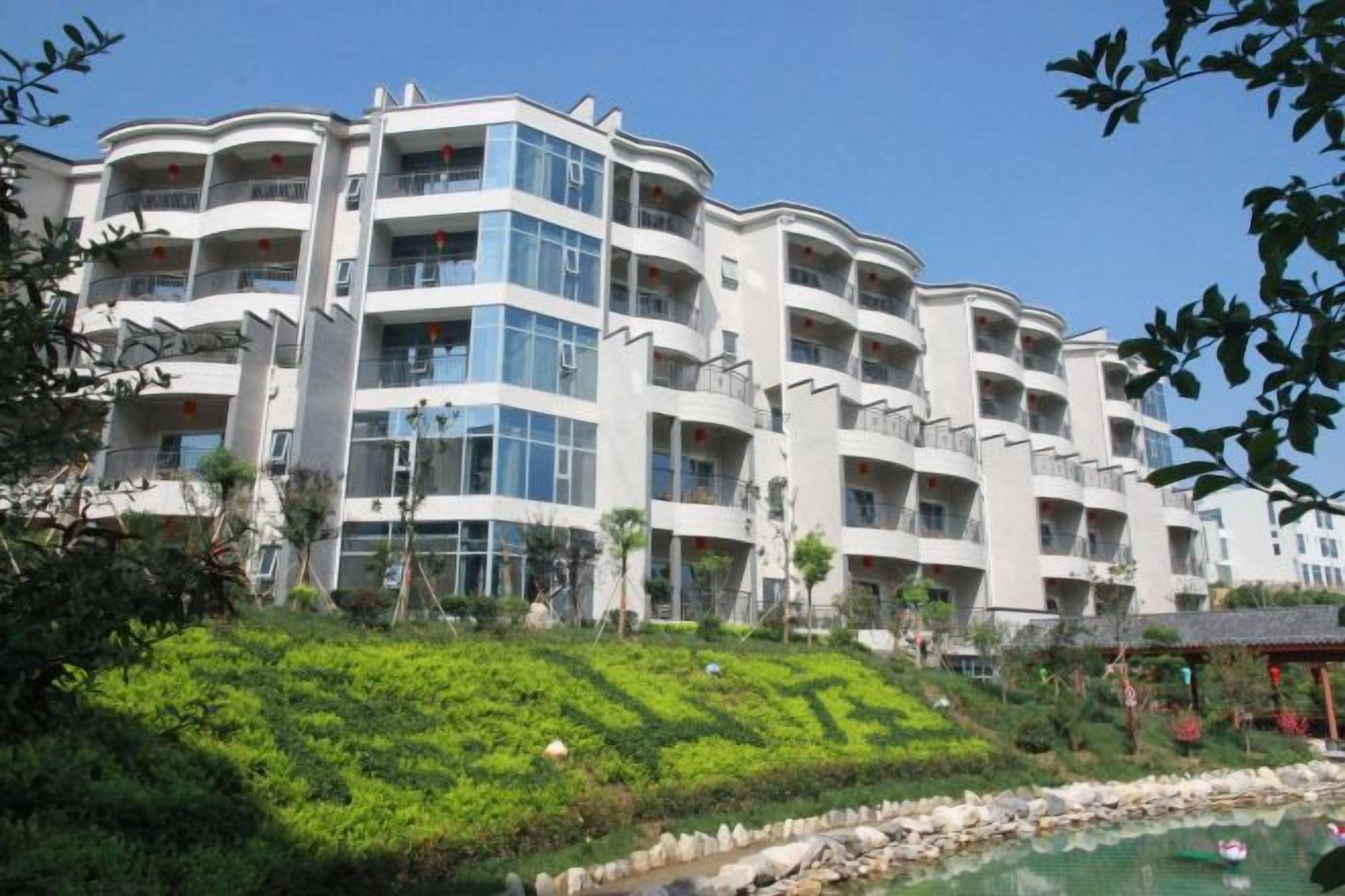 A multi-story hotel with balconies, a landscaped garden, and a swimming pool.