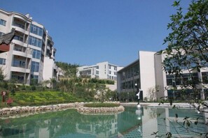 Ein modernes Hotel mit Schwimmbad, umgeben von Grünflächen und angrenzend an ein mehrstöckiges Gebäude.