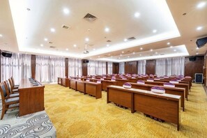 A conference room with rows of wooden tables and chairs, a carpeted floor, and a ceiling with recessed lighting.