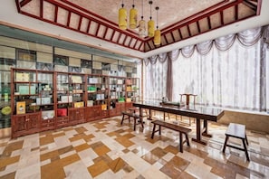 A spacious room with a large wooden bookshelf, a long dining table, and a view through large windows.