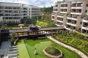 Un hotel con varios pisos, un patio con un pabellón tradicional y un estanque.
