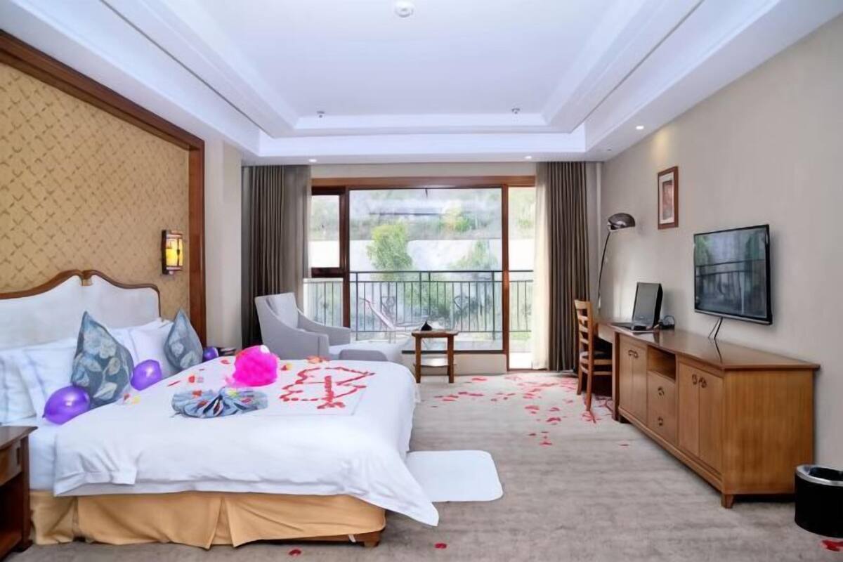 A hotel room with a bed, a desk, a chair, a TV, and a balcony.