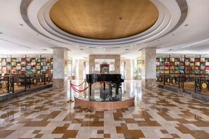 A spacious lobby with a central circular area, marble flooring, and bookshelves on either side.