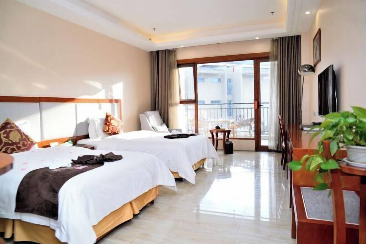 A hotel room with two beds, a balcony, a TV, and a dining area.