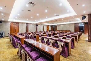 A conference room with rows of wooden tables and purple chairs, equipped with ceiling lights and a projector screen. - Tianlu Hotel (Shangnan)