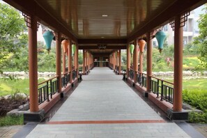 A covered walkway with columns and railings, leading to a garden area.