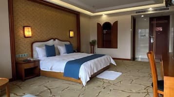 A hotel room with a large bed, a wooden nightstand, a desk, and a chair.