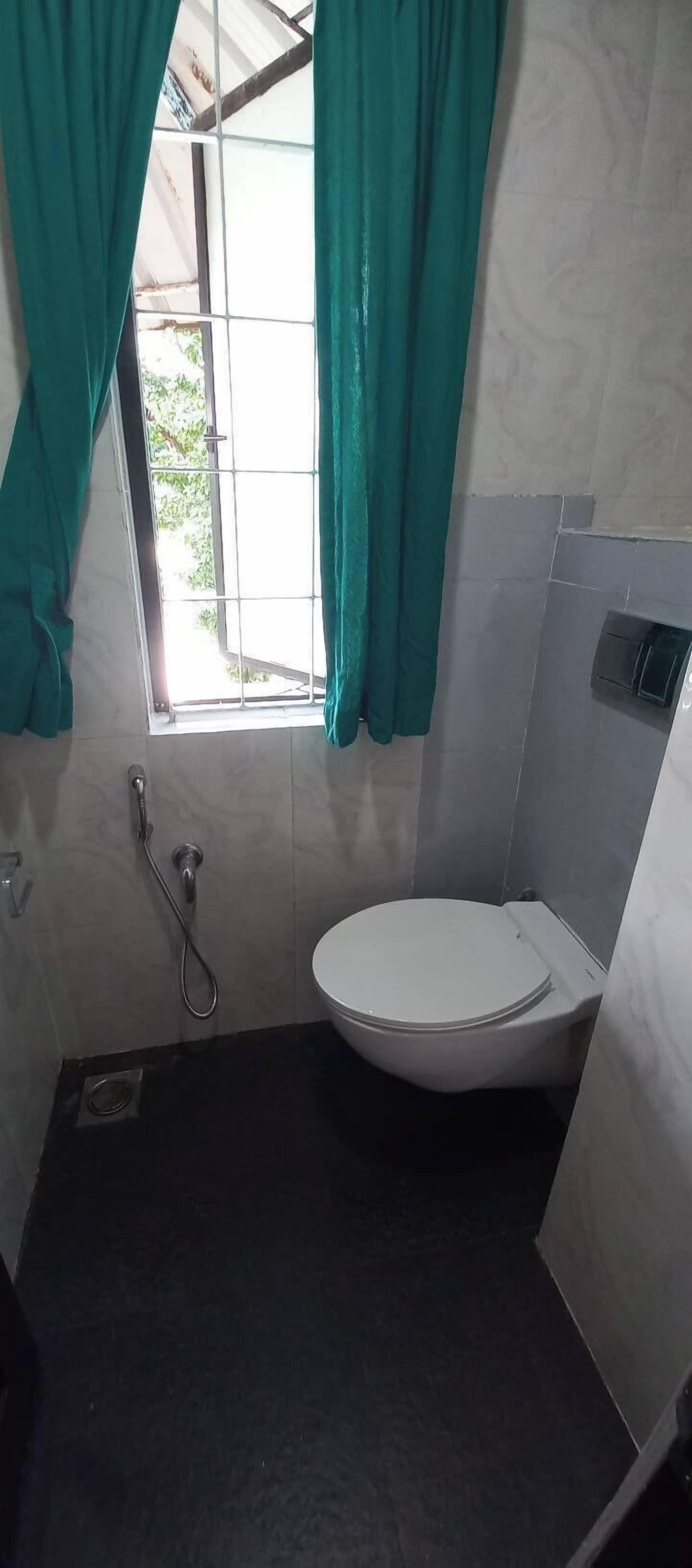 A small bathroom with a toilet, a shower, and a window with curtains.