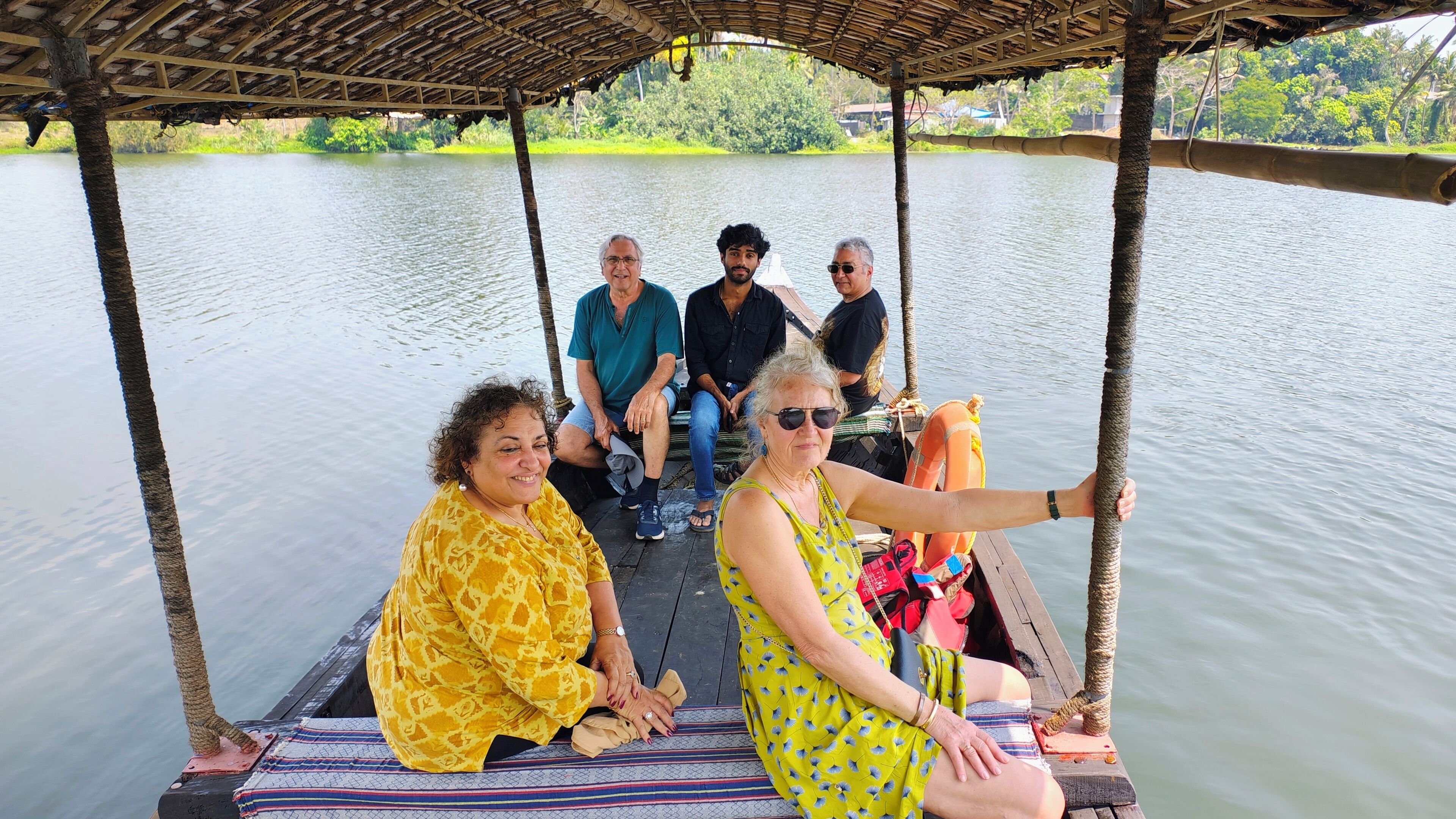 A group of people on a boat with a thatched roof, surrounded by calm water and greenery.