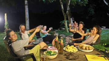 A group of people sitting around a table outdoors at night, holding drinks and toasting.
