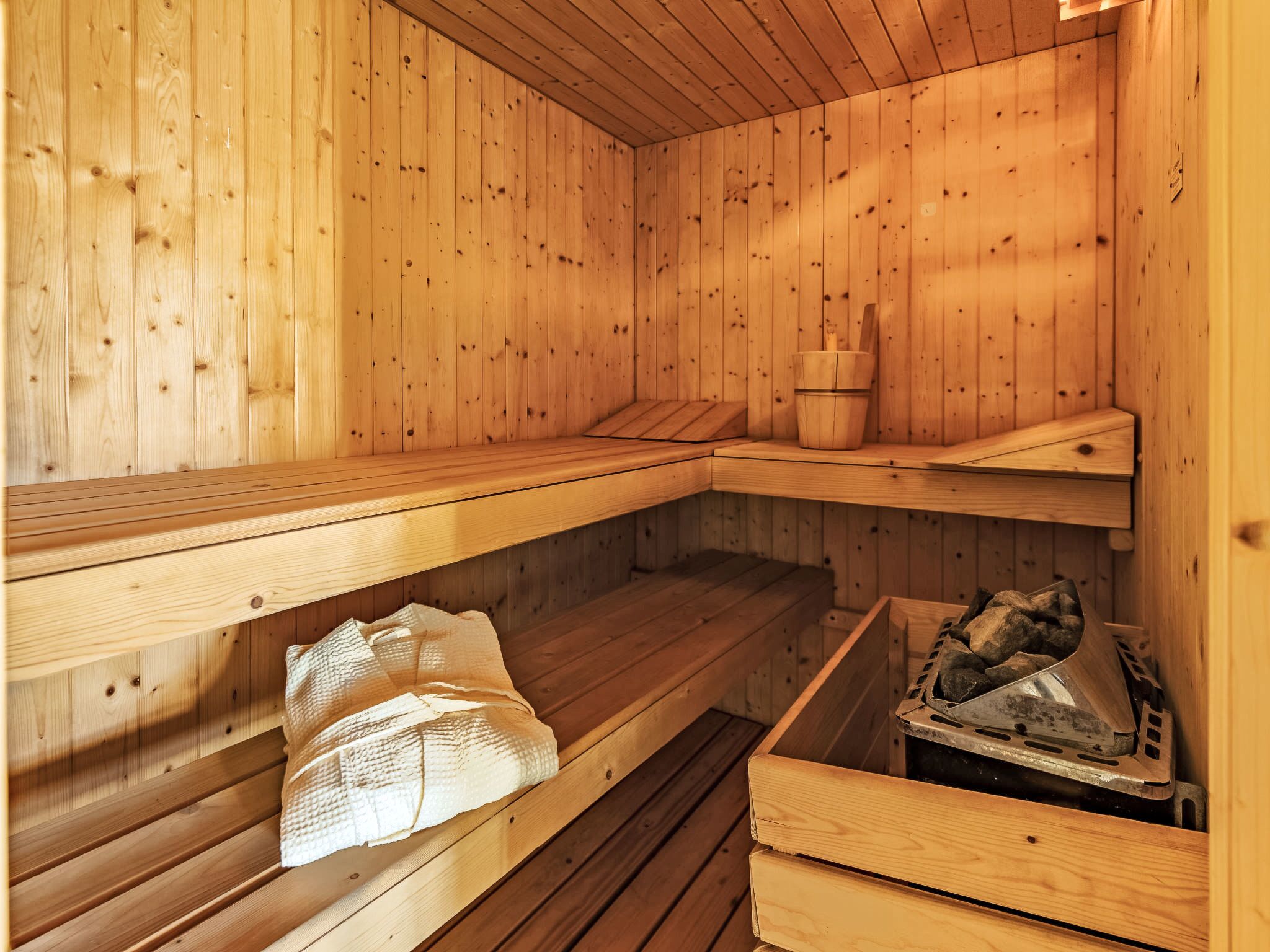 Un sauna en bois, avec des bancs, un seau et un récipient en métal.