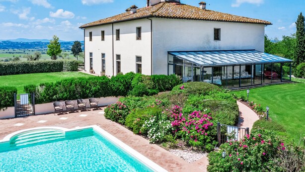 A large house with a swimming pool, surrounded by lush greenery and a clear blue sky.