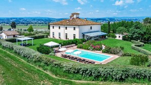 A large white villa with a tiled roof, a swimming pool, and a garden.