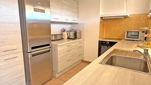A modern kitchen with stainless steel appliances, wooden cabinets, and a built-in dishwasher. - Apartment for 4 people - Air conditioning - WiFi - Downtown - Near shops - Sainte Maxime (STE MAXIME)