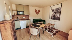 Een knus woongedeelte met een kitchenette, een eethoek met een ronde tafel, een groene bank en een groot stierenkunstwerk aan de muur.
