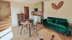 Een moderne woonkamer met een groene bank, een eettafel met stoelen, een keuken en een trap naar een hoger niveau.