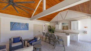 A spacious living area with a high ceiling, a kitchen with white cabinets, and a dining area with wicker furniture. - 66 Palmetto Lane located in Ocean Oaks on Jekyll (Jekyll Island)