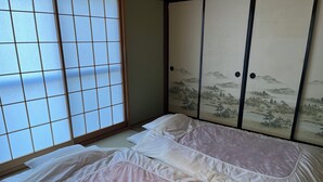 Ein traditioneller japanischer Raum mit Tatami-Boden, einer Futon-Liege, Shoji-Schiebebildschirmen und einer gleitenden Tür mit Landschaftsbild.