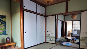 Ein traditioneller japanischer Raum mit Tatami-Böden, Schiebetüren und Blick auf einen Garten durch einen Papierbildschirm.